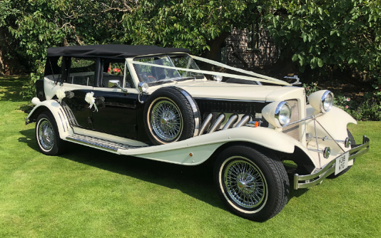 A black and white Beauford wedding Car parked on grass